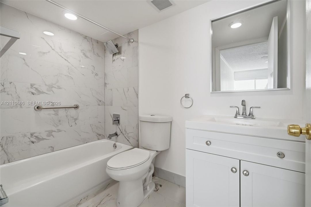Full-height tub enclosure with stone-pattern tile surround, white vanity cabinet with integrated sink, polished chrome plumbing fixtures, and rectangular wall mirror