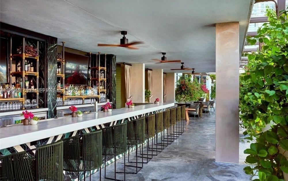 Covered outdoor bar featuring a white countertop, stone-tiled back wall with integrated shelving, recessed ceiling fans, and concrete flooring