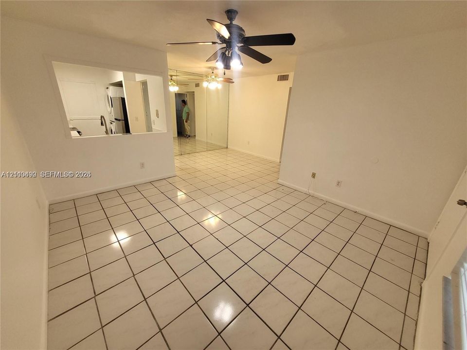Open-concept interior featuring large-format ceramic tile flooring, a pass-through wall opening, mirrored wall panels, and ceiling-mounted fans