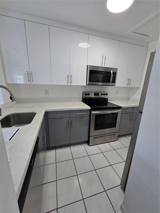 Kitchen featuring white flat-panel cabinetry, stainless steel appliances, a stone-composite countertop, an integrated undermount sink, and tiled flooring