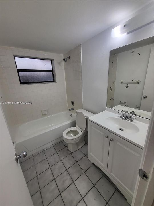 Bathroom featuring a white vanity cabinet with an integrated sink, a built-in shower and tub combination with wall tiling, and ceramic floor tile