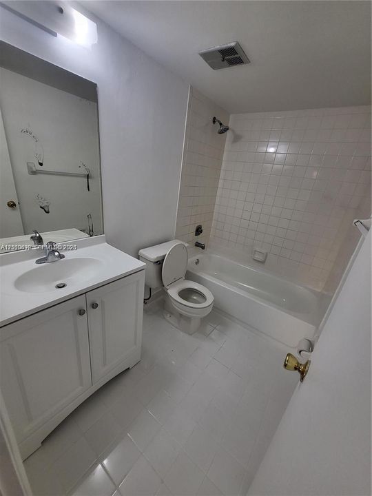 Bathroom featuring white cabinetry, integrated sink, large wall-mounted mirror, and tiled shower-tub combination