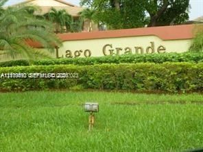 Stucco-finished community monument sign featuring raised lettering, surrounded by manicured hedges, palm trees, and established landscaping