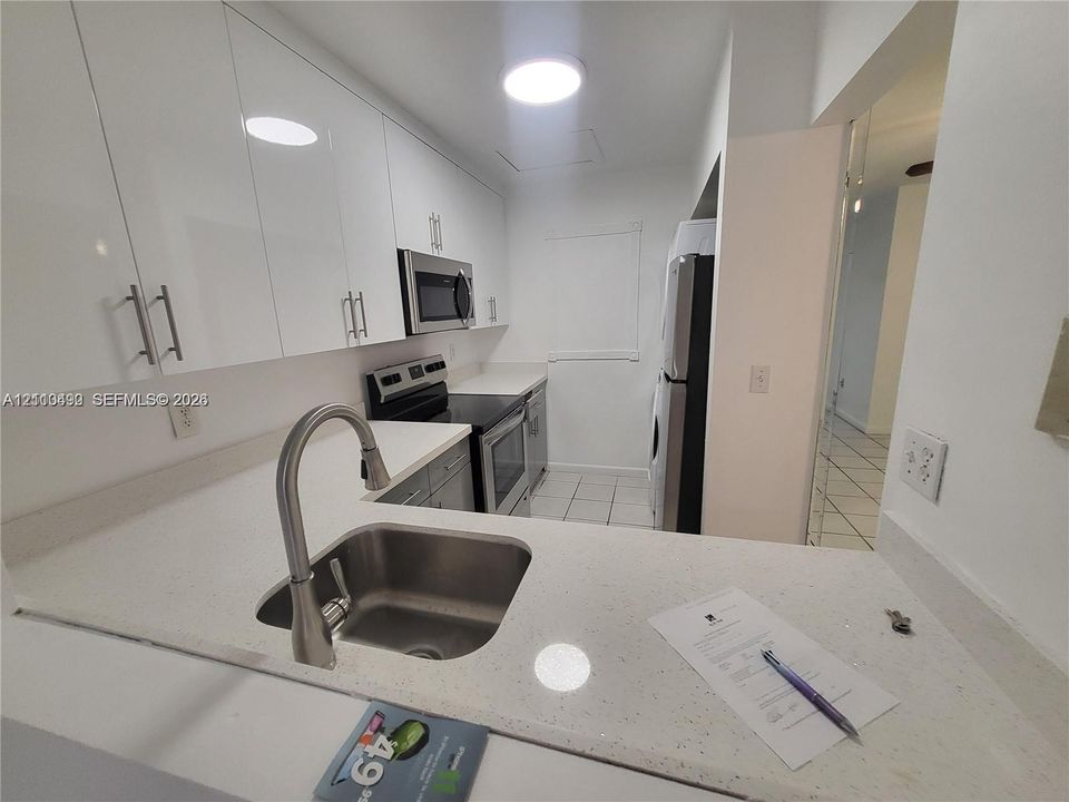 Kitchen featuring white high-gloss cabinetry, stone-finish countertops, stainless steel undermount sink with arched faucet, and integrated stainless steel appliances