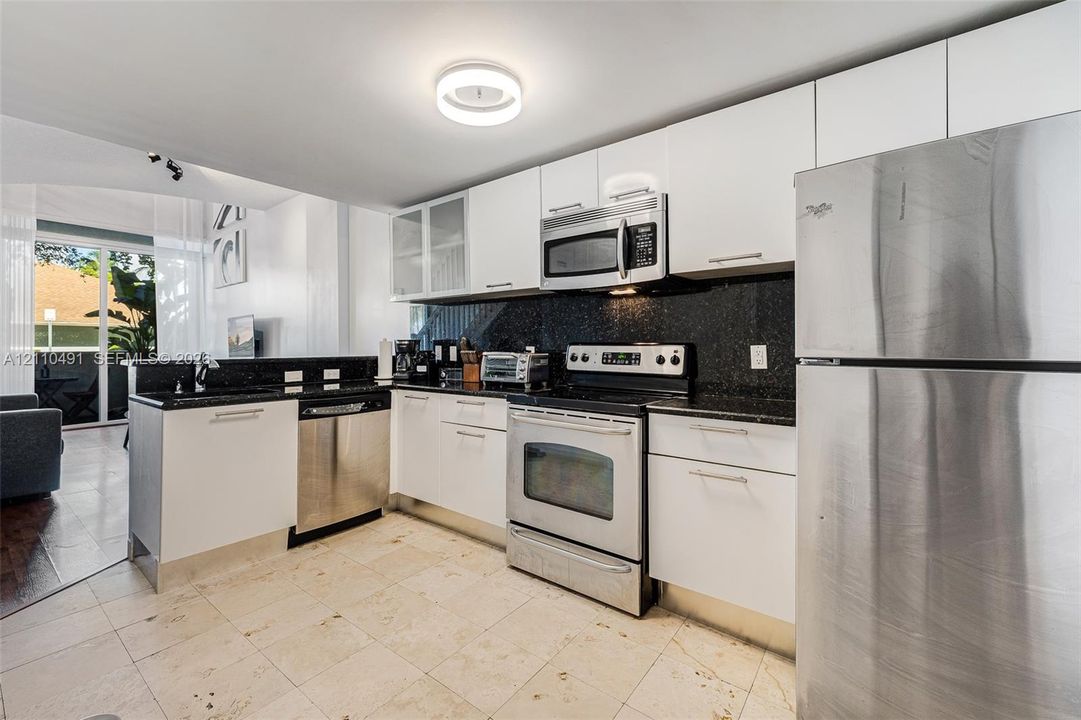Kitchen featuring flat-panel white cabinetry, stone-finish countertops, stainless steel appliances, and tile flooring