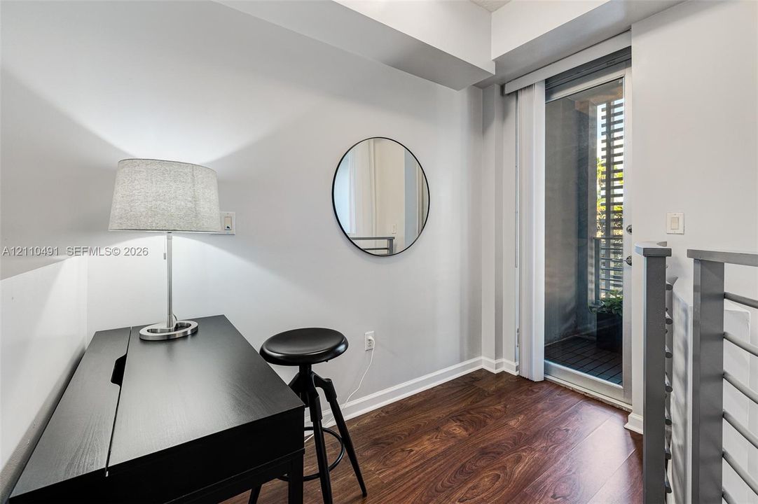 Wood-finish flooring, wall-mounted circular mirror, and glass-paneled door leading to an exterior balcony with metal railing