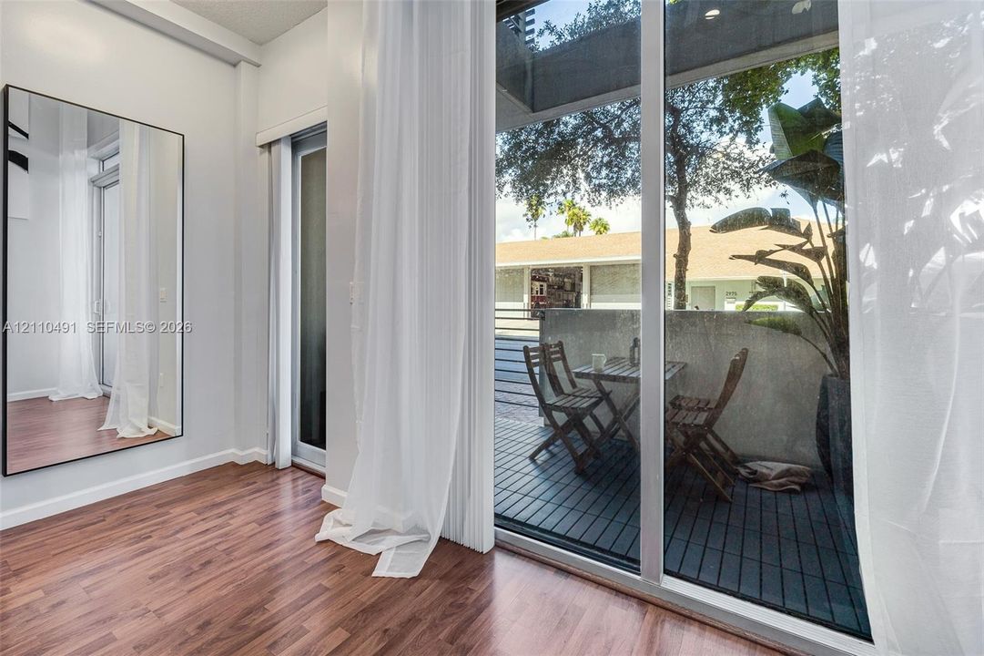 Full-height wall mirror, wood-finish flooring, floor-to-ceiling glass sliding door, and private exterior balcony with slatted decking