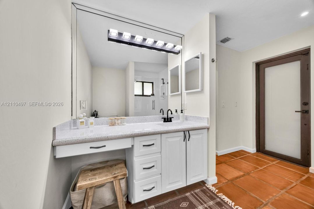 Bathroom vanity featuring white cabinetry, stone-composite countertop, integrated sink, matte black faucet, and full-width wall mirror with integrated lighting