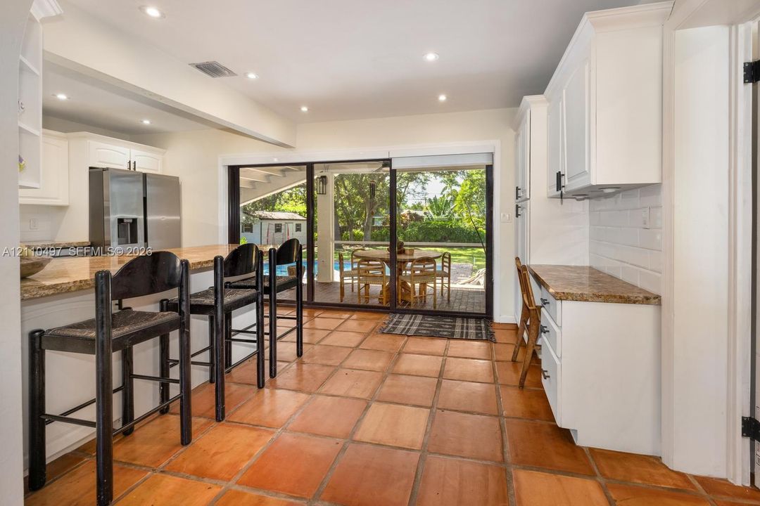 Kitchen featuring a stone-topped breakfast bar, recessed ceiling lighting, white cabinetry, tile flooring, and a sliding glass door
