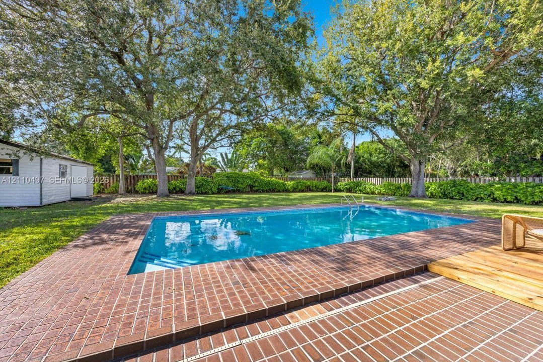 Backyard swimming pool with a brick paver deck, detached storage structure, mature trees, and privacy fencing