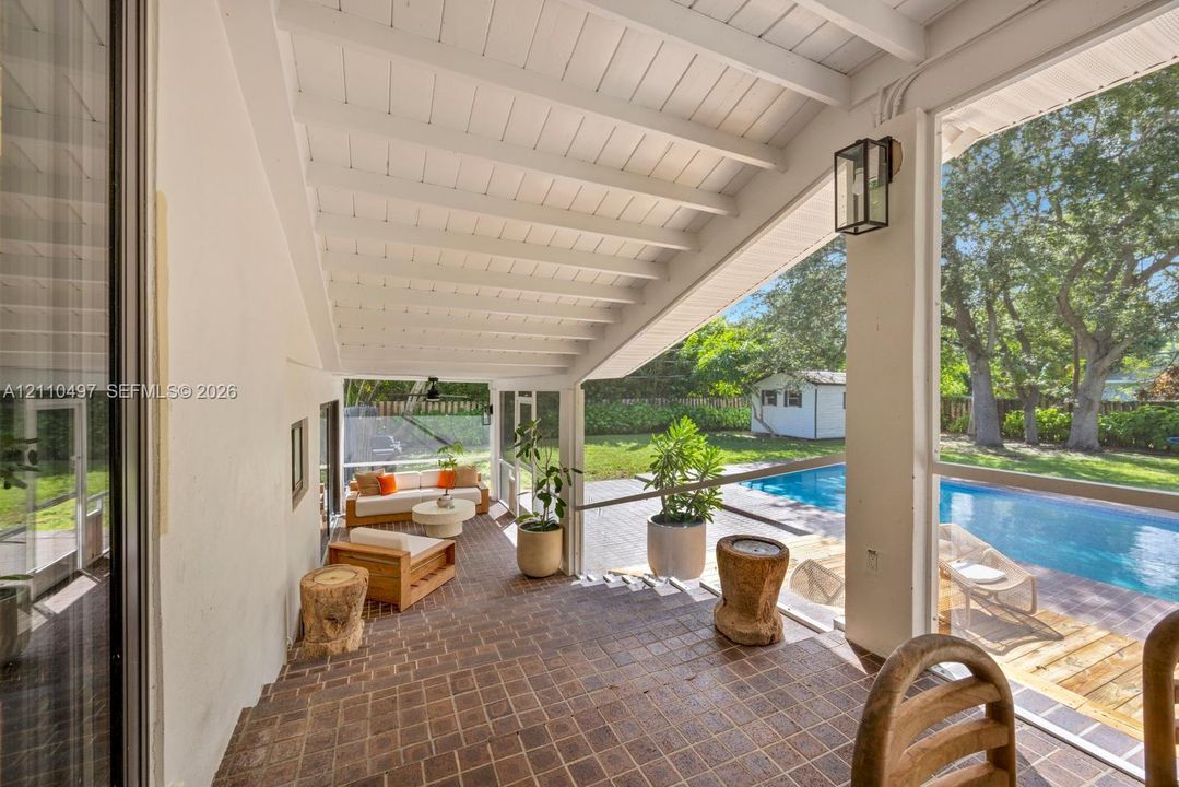 Screened-in lanai featuring a brick floor, painted wood-beam ceiling, attached wall-mounted lantern lighting, and an inground pool with a wood-plank deck