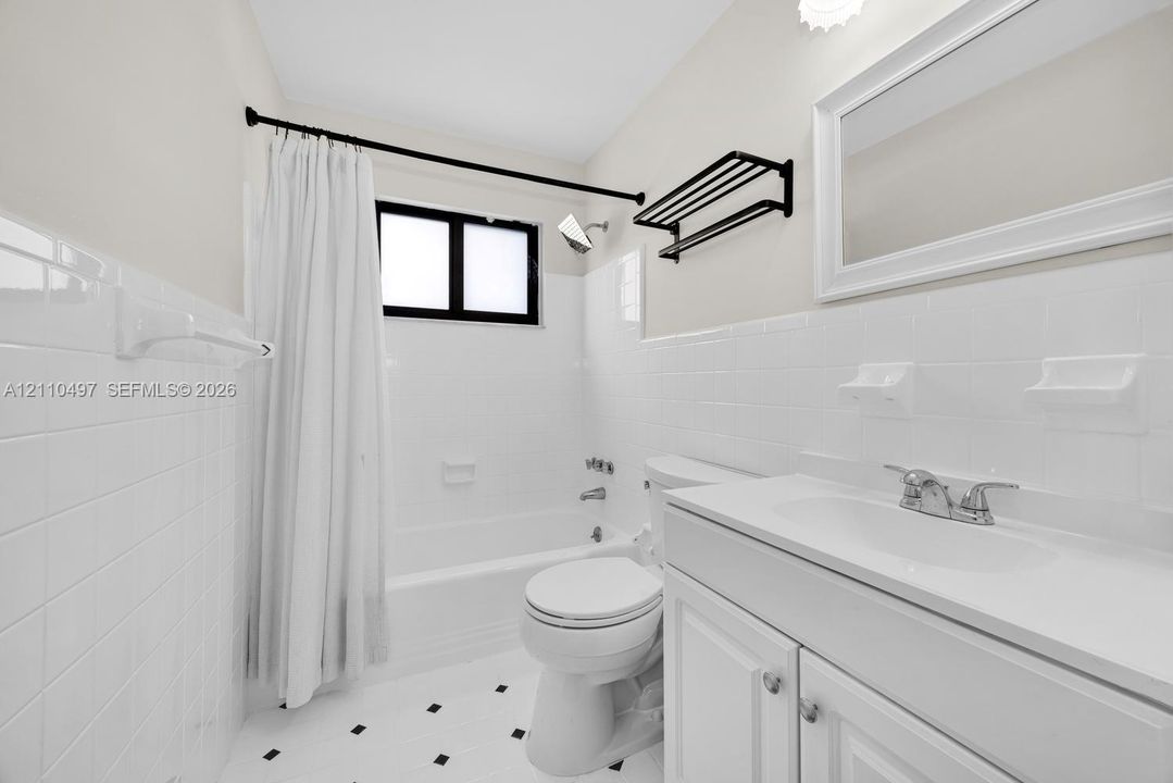 Bathroom featuring a white vanity cabinet with an integrated sink, white subway tile wall surround, black-framed shower curtain rod, wall-mounted storage rack, and tile flooring with a geometric accent pattern