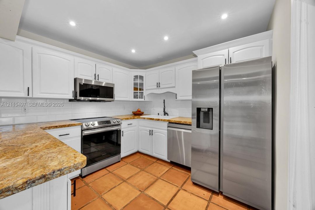 Kitchen featuring white cabinetry, stone countertops, stainless steel appliances, white subway tile backsplash, and terracotta-style flooring