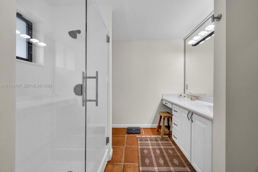 Walk-in shower with a glass enclosure, vanity with stone-style countertop, undermount sink, and wall-to-wall mirror