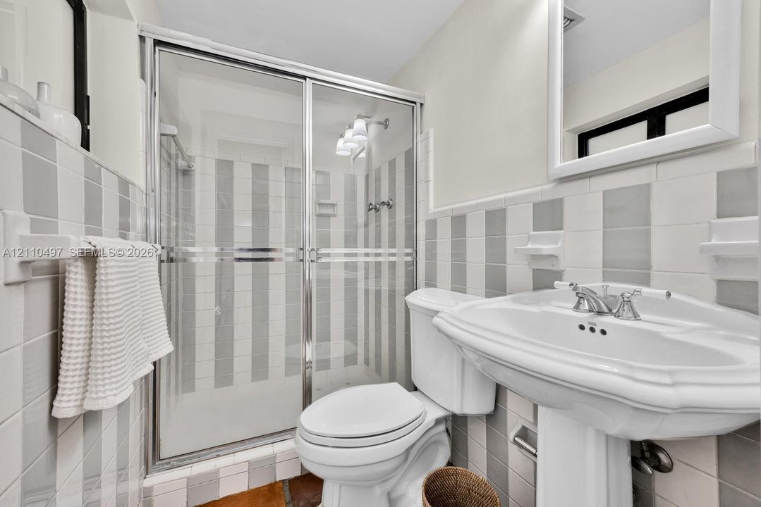 Bathroom featuring a pedestal sink with a chrome dual-handle faucet, a walk-in shower with a glass sliding enclosure, a framed wall mirror, and vertically-striped tile wall detailing