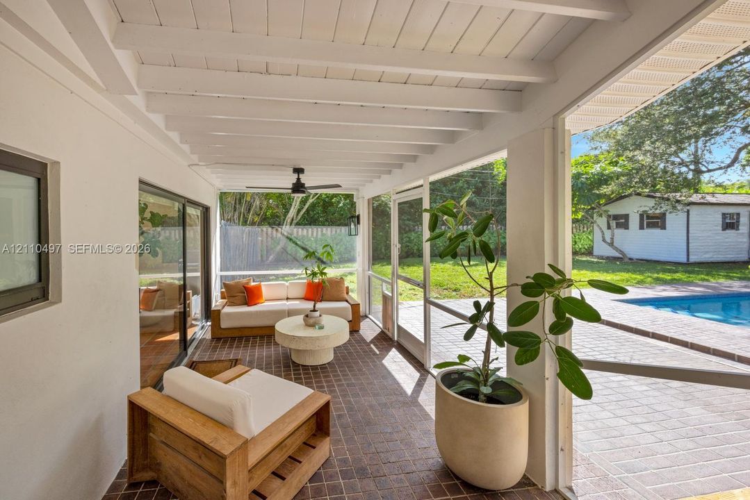 Screened-in patio featuring a vaulted ceiling with exposed beams, ceiling fan, dark tile flooring, and direct exterior access to a paved pool deck