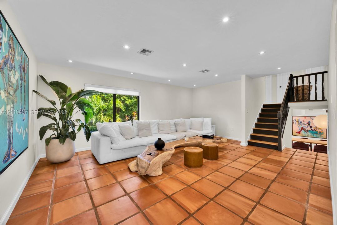 Living area featuring terra-cotta tile flooring, recessed ceiling lighting, and a staircase with a dark-finished wooden handrail and balusters