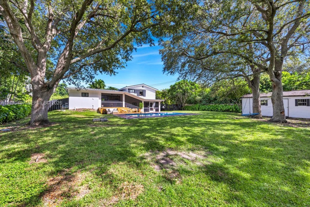 Expansive backyard featuring a rectangular swimming pool, wood-decked patio, mature trees, and an accessory storage structure