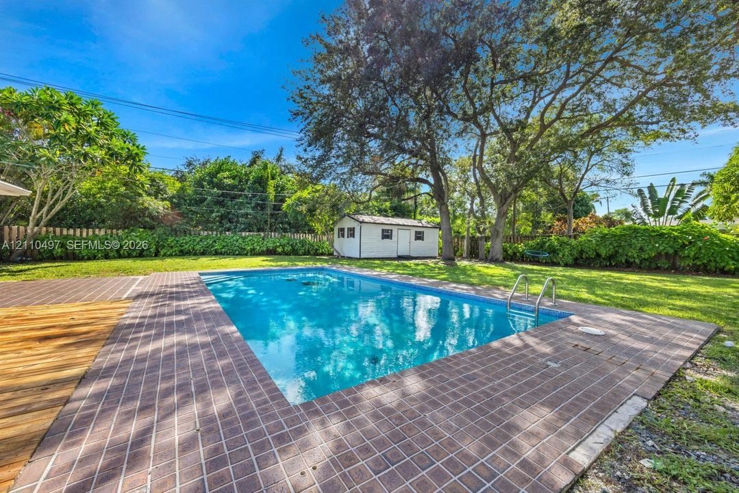 Outdoor space featuring an in-ground swimming pool, tiled pool deck, expansive lawn, mature trees, and an accessory storage structure