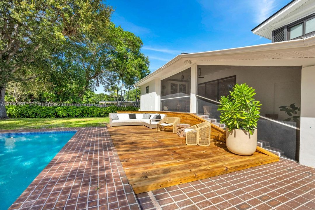 Outdoor living space featuring a raised wood deck, tiled pool surround, swimming pool, and screened-in porch