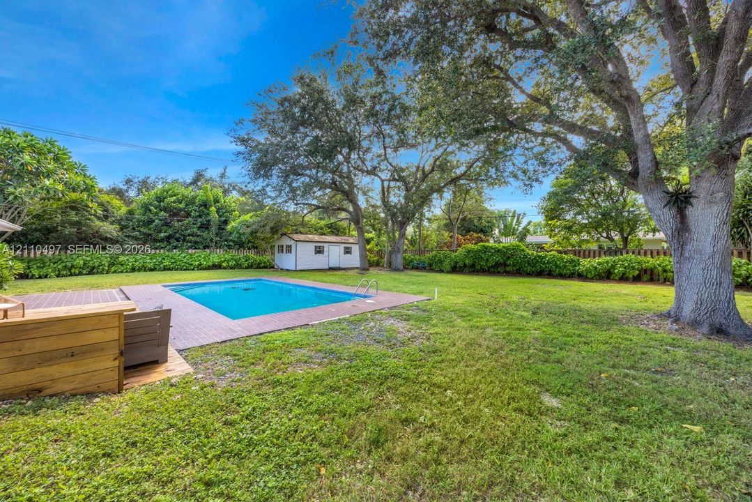 Spacious backyard featuring an in-ground swimming pool, brick paver decking, mature oak trees, and a detached storage structure