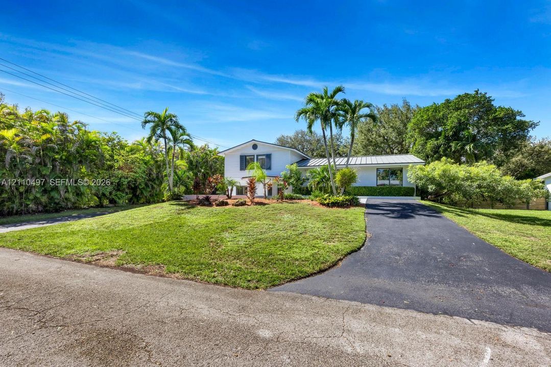 Single-story residence featuring a white exterior, a metal roof, an asphalt driveway, and mature landscaping with palm trees