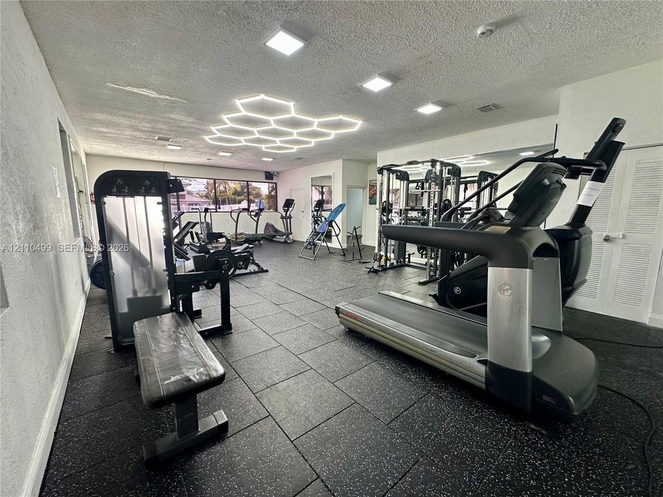 Fitness center featuring durable rubberized flooring, large-scale wall-mounted mirrors, recessed LED lighting, and a prominent hexagonal ceiling light fixture