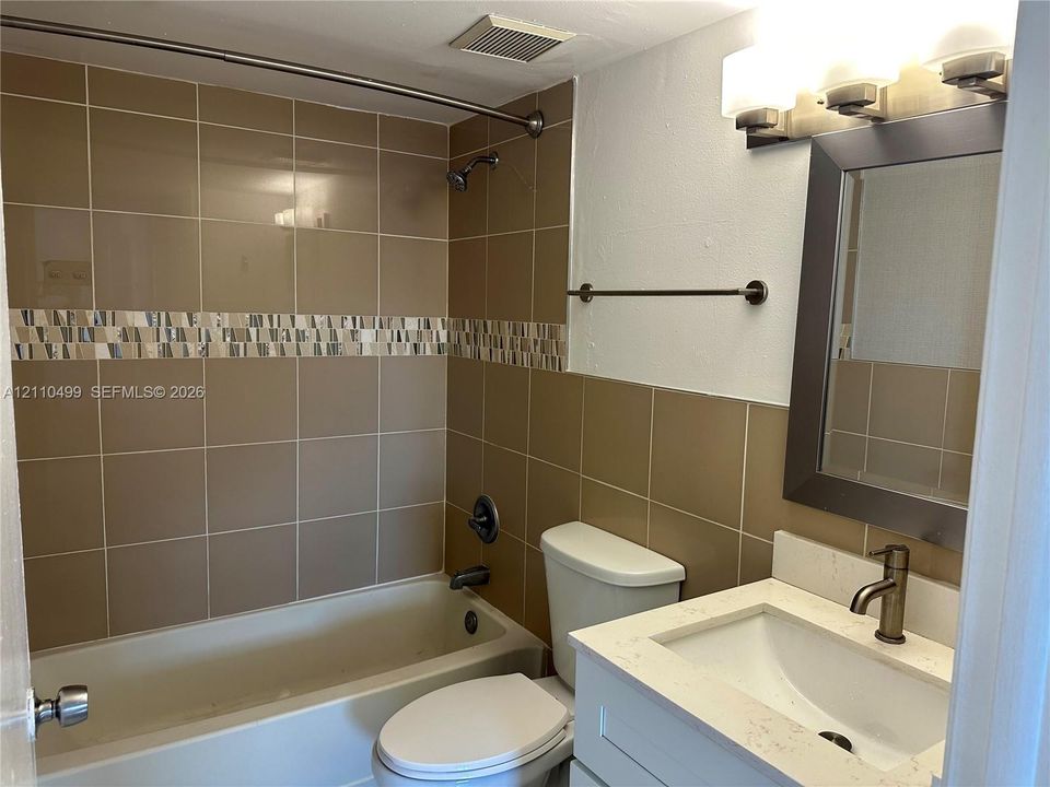 Bathroom featuring a tub and shower combination with tile surround and decorative accent border, white vanity with stone-finish countertop, undermount sink, and wall-mounted vanity light