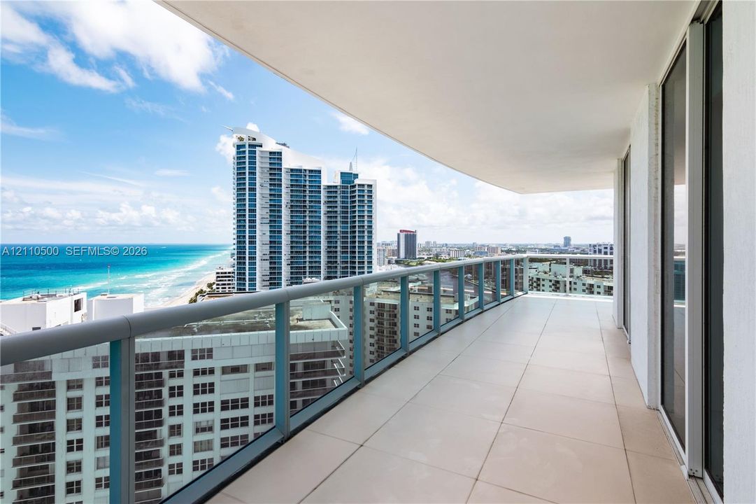 Expansive balcony featuring large-format tile flooring, a glass-panel railing, and panoramic coastal and urban scenery