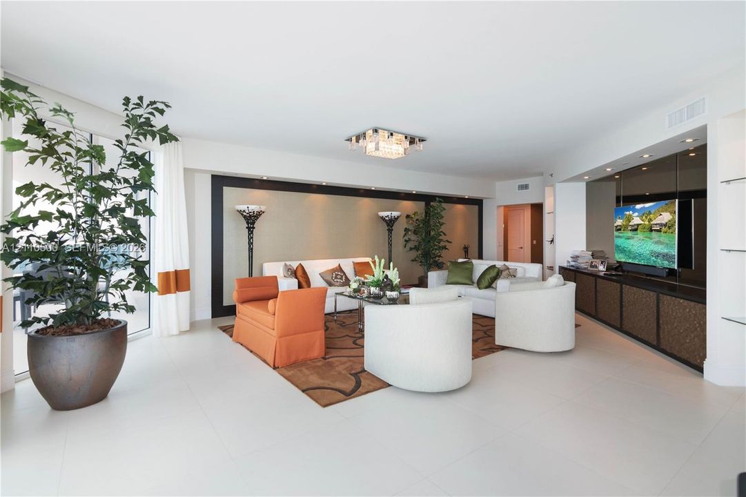 Living area featuring oversized floor-to-ceiling windows, large-format tile flooring, built-in entertainment cabinetry with integrated recessed lighting, and a tiered crystalline flush-mount ceiling fixture