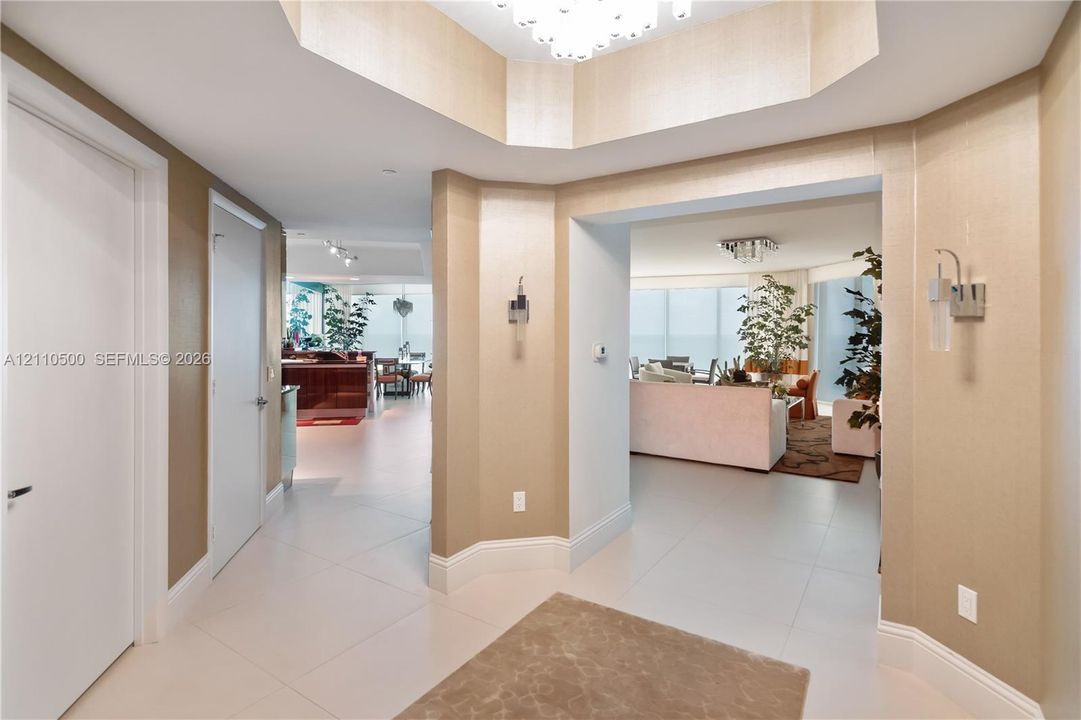 Foyer featuring a recessed tray ceiling, large-format tile flooring, textured wall finishes, and wall-mounted metal sconces