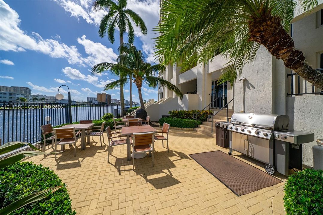 Patio featuring herringbone-patterned pavers, built-in stainless steel grill, metal fencing, and mature palm trees