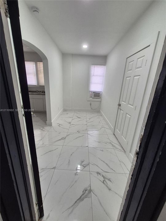 Interior space featuring polished large-format tile flooring with veining, an arched passage, a six-panel door, recessed lighting, and a window with a built-in wall air conditioning unit