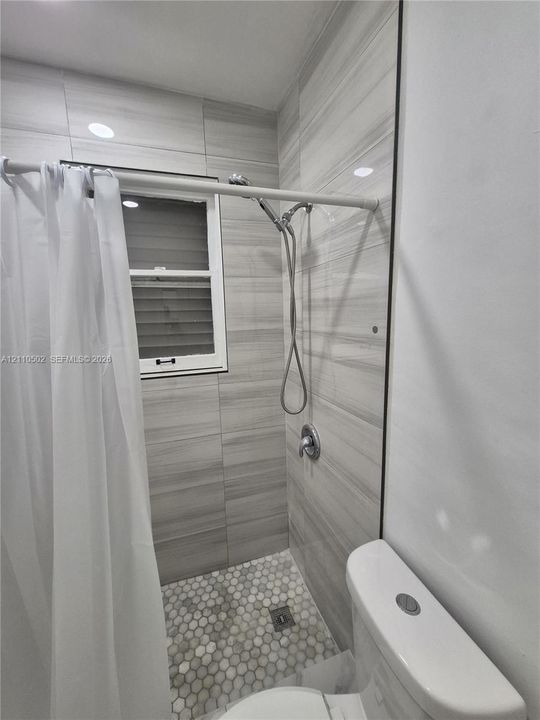 Shower enclosure featuring large-format horizontal wall tile, hexagonal floor tile, chrome shower fixture, and a single-hung window