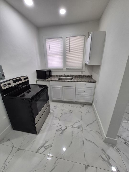Kitchen featuring white cabinetry, stone-finish countertops, stainless steel sink, large-format tile flooring, and recessed ceiling lighting