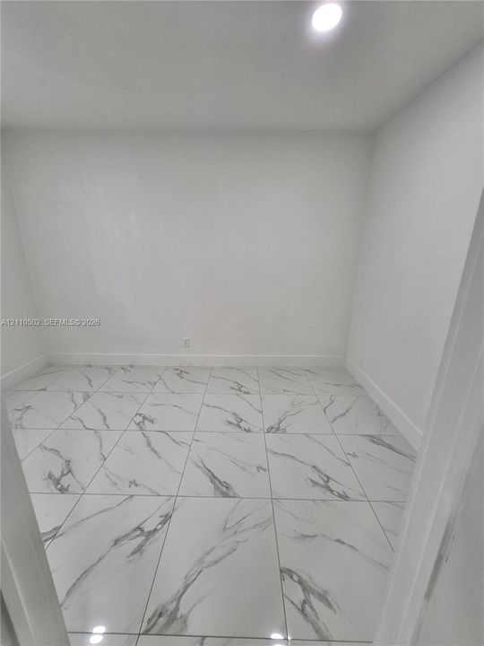 Large-format tile flooring with a neutral veined pattern, crisp white walls, and integrated recessed ceiling lighting