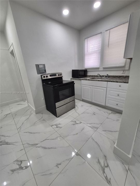 Kitchen featuring large-format veined tile flooring, white shaker-style cabinetry, high-contrast countertop, and stainless steel range