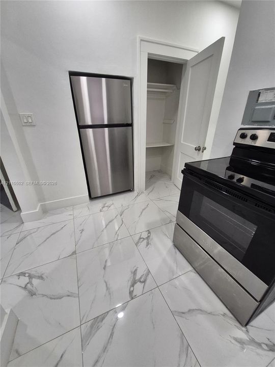 Large-format tile flooring with a marble-patterned finish, stainless steel refrigerator, black and stainless steel range, and built-in closet with shelving
