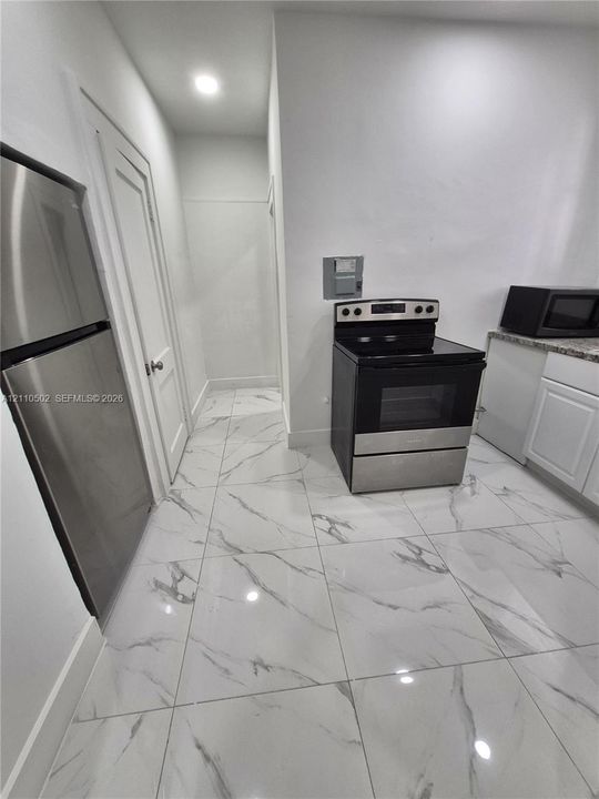 Kitchen featuring large-format veined tile flooring, stainless steel appliances, white cabinetry, and a stone-finish countertop