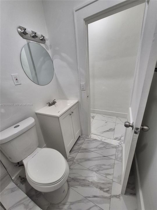 White vanity cabinet with an integrated rectangular sink, wall-mounted oval mirror, three-light polished chrome vanity fixture, and large-format porcelain tile flooring with veining
