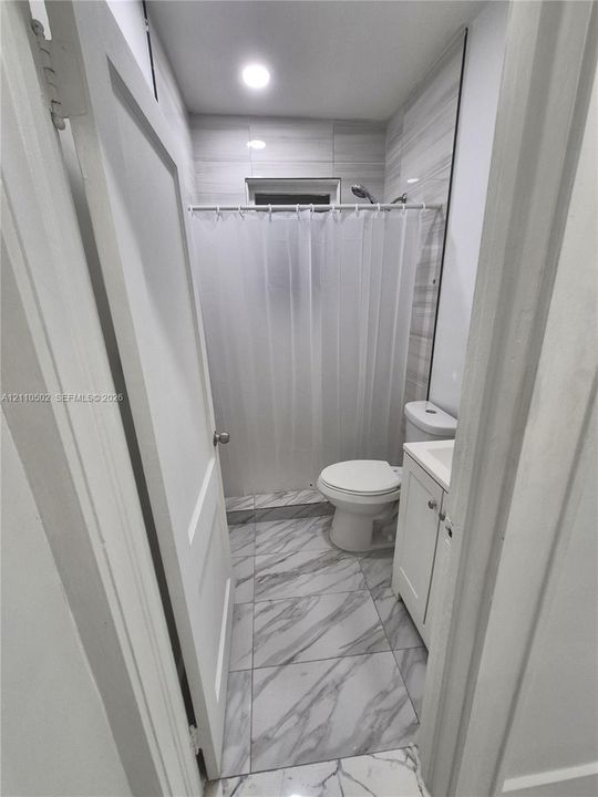 Bathroom featuring large-format veined tile flooring, white vanity cabinet with integrated sink, recessed lighting, and wall-mounted shower surround with horizontal tile detailing