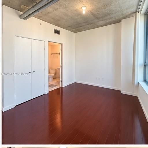 Exposed concrete ceiling, dark wood-finish flooring, floor-to-ceiling windows, and double-door closet