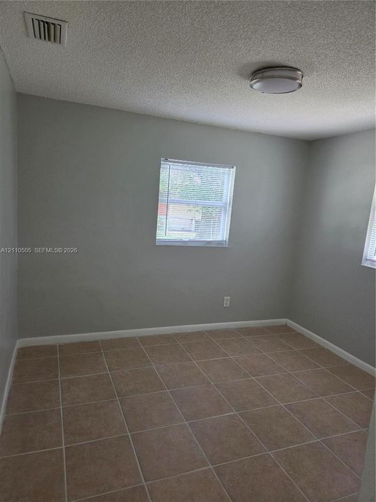 Neutral-toned interior space featuring light-colored tile flooring, smooth walls, and two windows with horizontal blinds