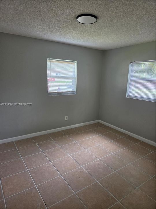 Neutral-toned room featuring tiled flooring, two windows with horizontal blinds, and a flush-mount ceiling light fixture