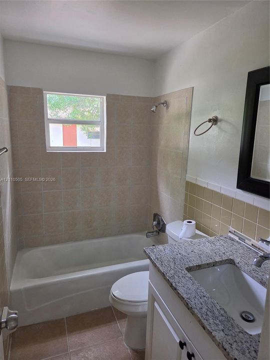 Bathroom featuring a vanity with a stone-finish countertop, undermount sink, built-in cabinetry, ceramic tile shower surround, and tile flooring