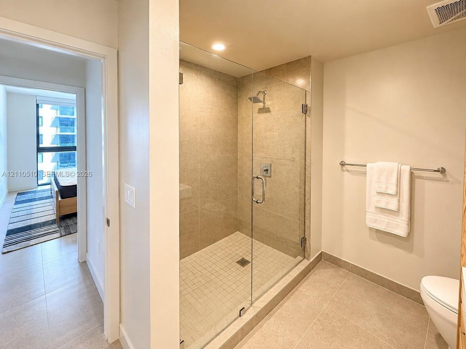 Walk-in shower featuring glass paneling, floor-to-ceiling stone-tile surround, square mosaic tile flooring, and a wall-mounted shower fixture