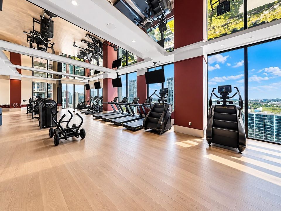 Fitness center featuring floor-to-ceiling windows, wood-finish flooring, mirrored ceiling accents, and structural columns