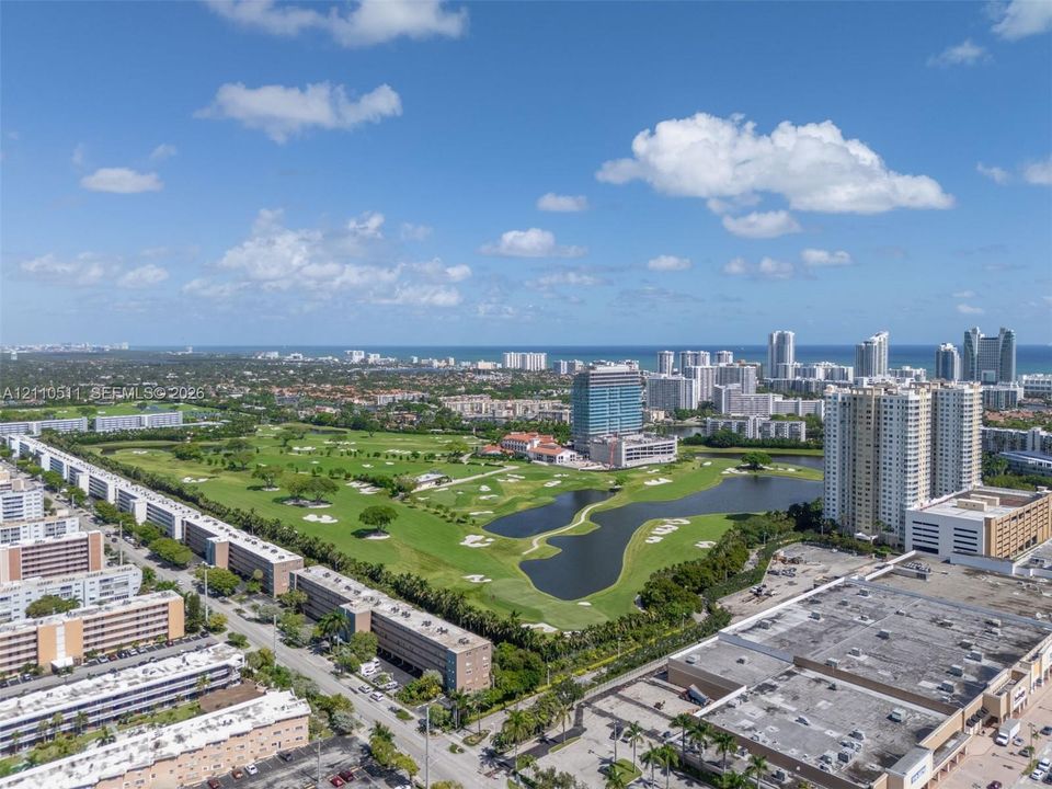 Aerial perspective of a golf course featuring expansive green fairways, sand bunkers, multiple water hazards, and mature tree clusters