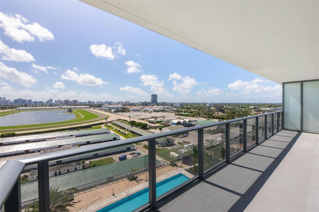 Covered balcony featuring a glass and metal railing, concrete flooring, and an expansive cityscape backdrop