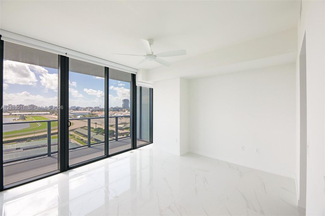 Primary suite with floor-to-ceiling sliding glass doors, white stone-finish flooring, white ceiling fan, and black-framed balcony railing